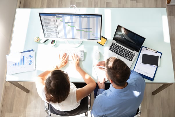 Vista superior de dois profissionais analisando planilhas e gráficos no computador